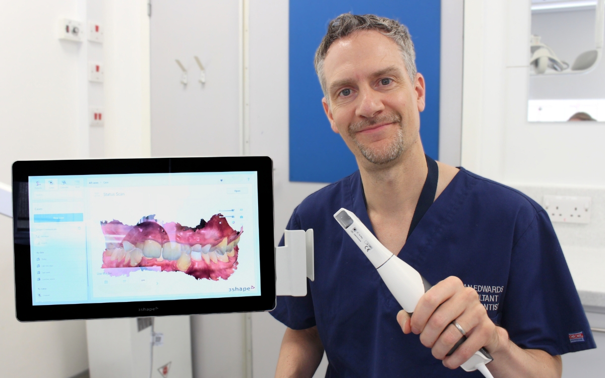 Consultant Orthodontist, wearing blue uniform, showing the new intraoral digital scanner. On the screen new to them there is a 3D image of a patients teeth. 
