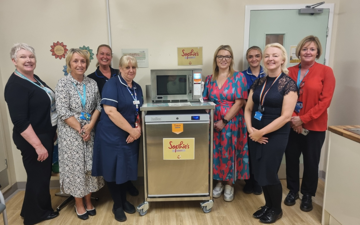 Group of staff stood with microwave and fridge.