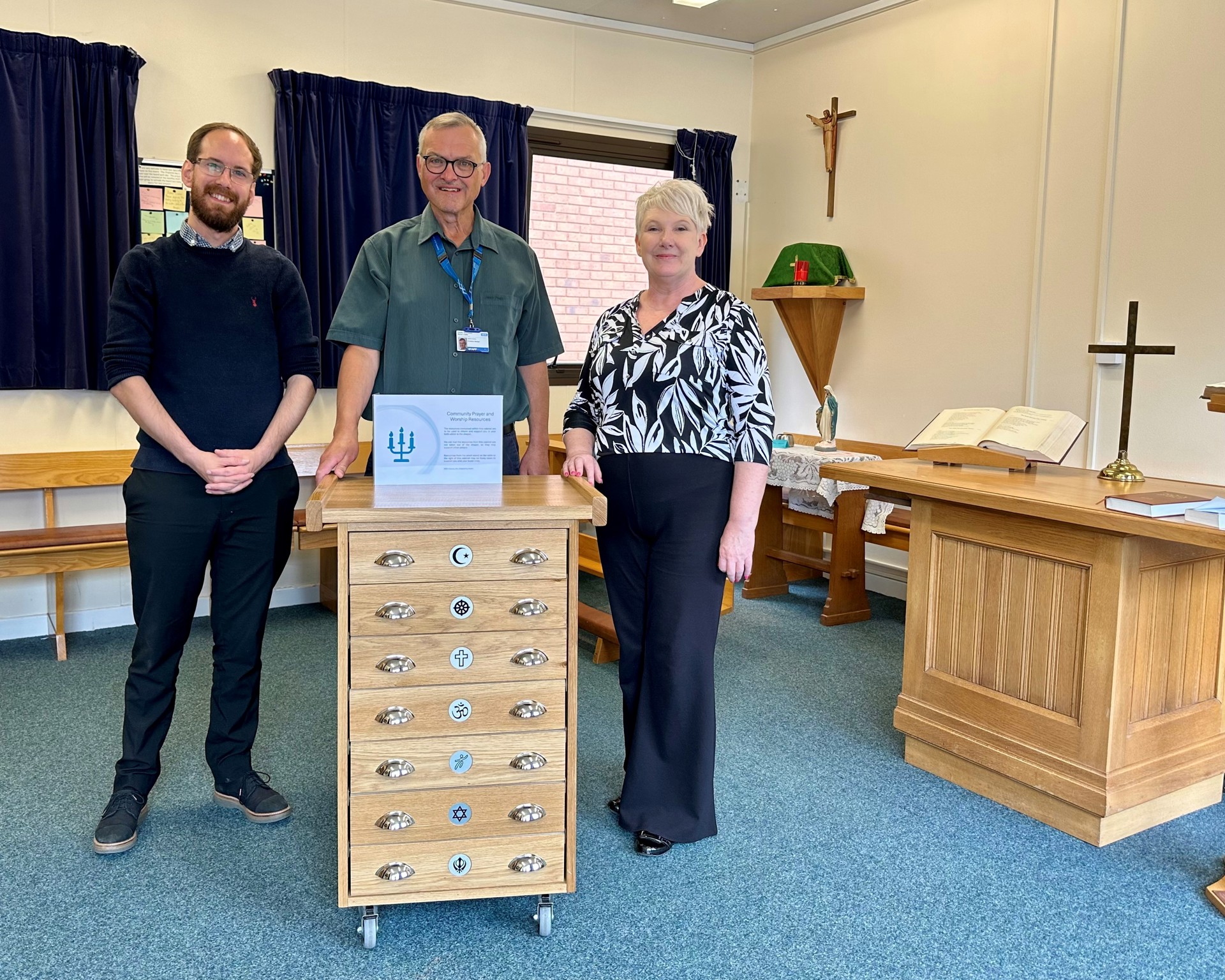Paul Klein, David Lowery and Helen Higginson posing with the seven drawer multi-faith cabinet.