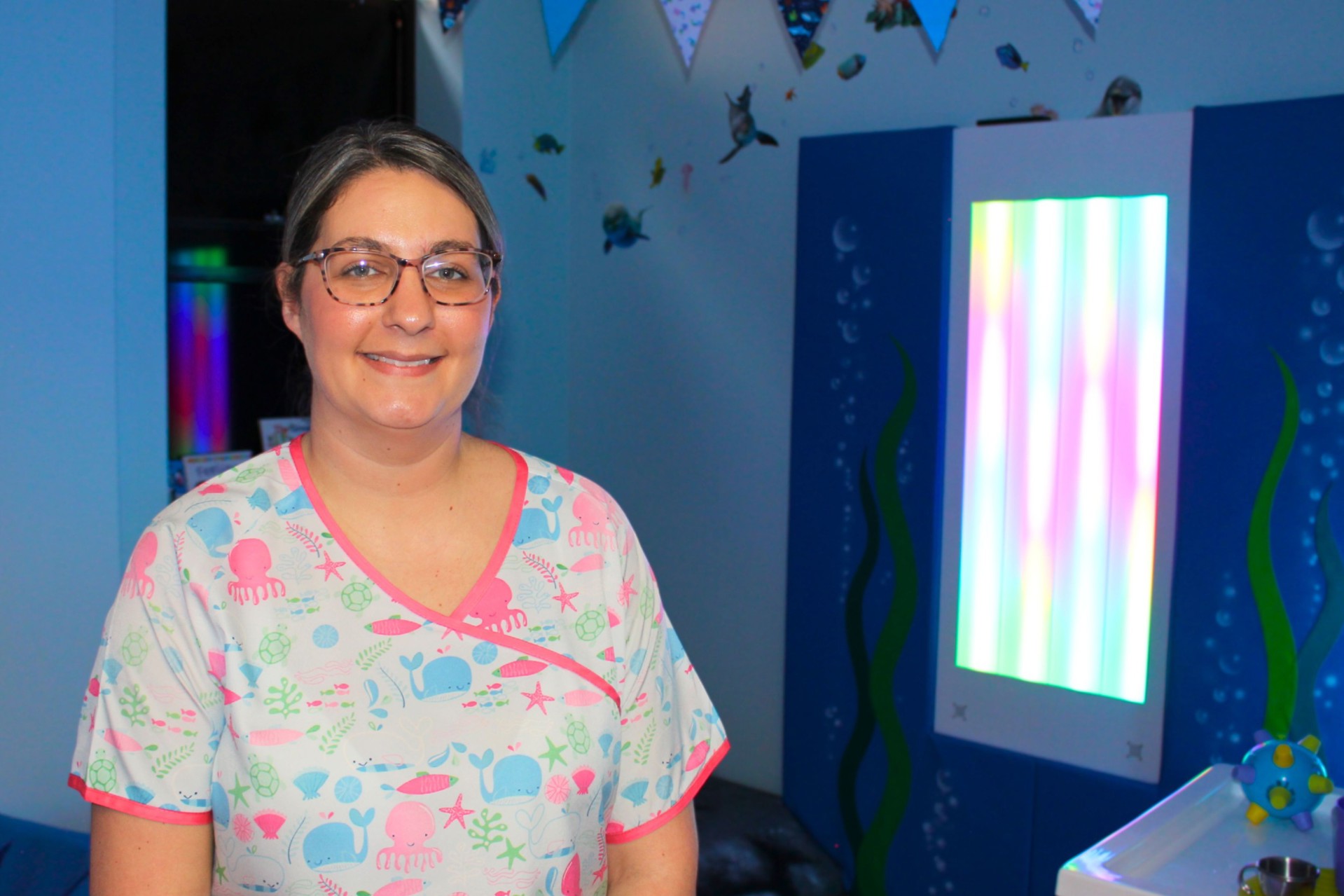 Child play specialist smiling in front of the sensory room at Warrington Hospital.